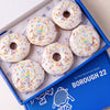 Gluten free vegan unicorn doughnuts with white icing, pastel sprinkles and rainbow unicorn horn toppers in a Borough 22 box